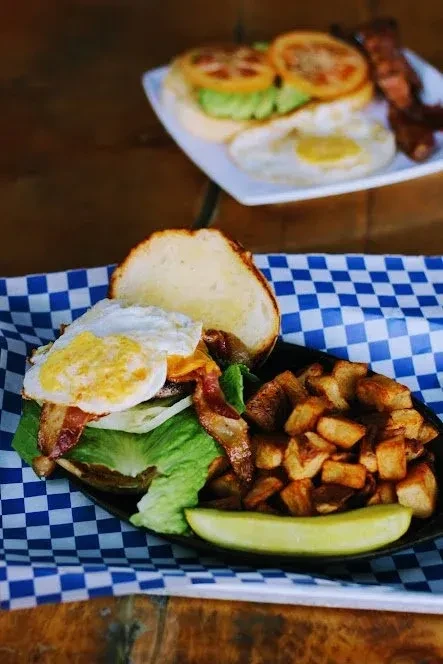 Close-up: open-faced breakfast sandwich, egg, bacon, potatoes, and pickle.