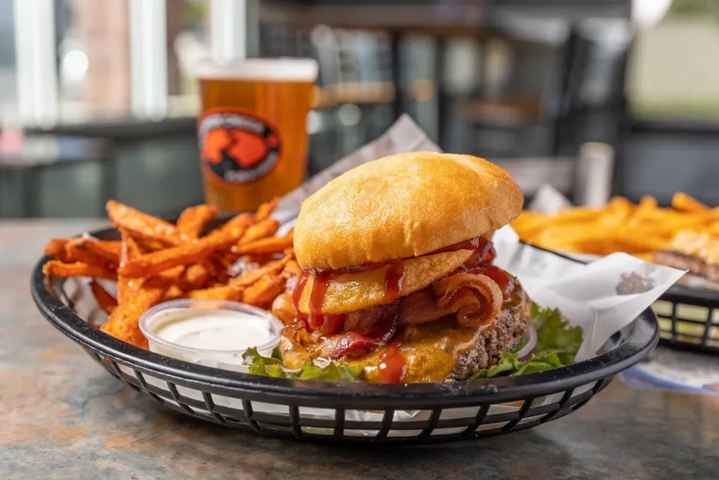 Burger with bacon, onion rings, sweet potato fries, and dipping sauce.