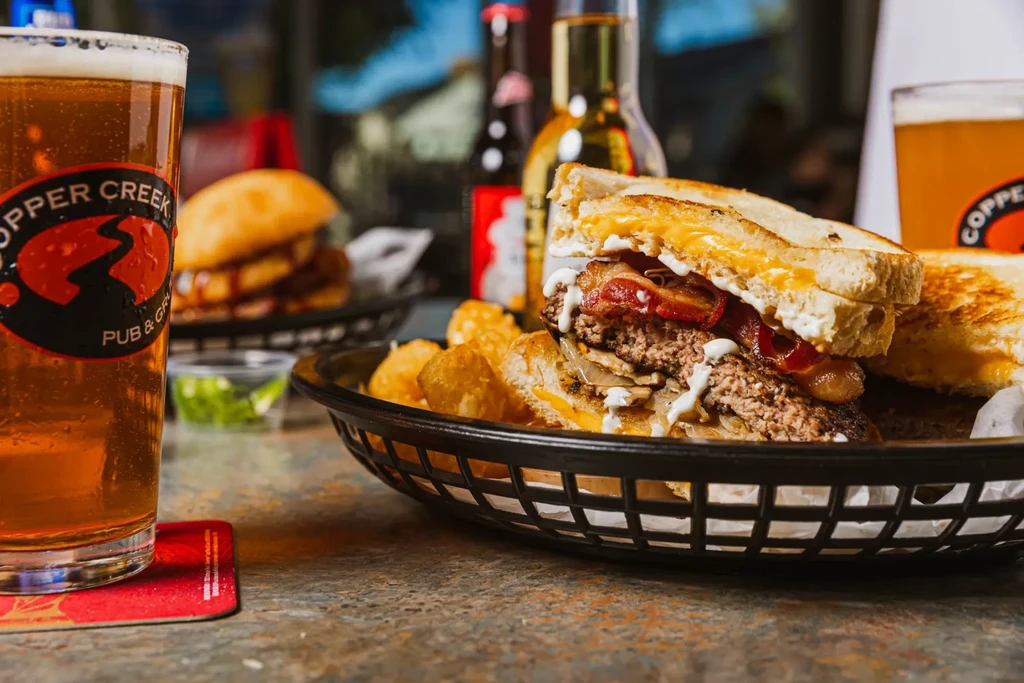 Close-up of Copper Creek beer, beef patty melt, and tater tots.