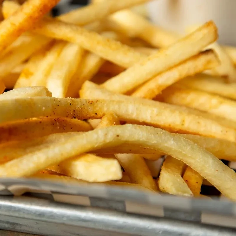 Crispy, golden-brown french fries with seasoning in a checkered tray.