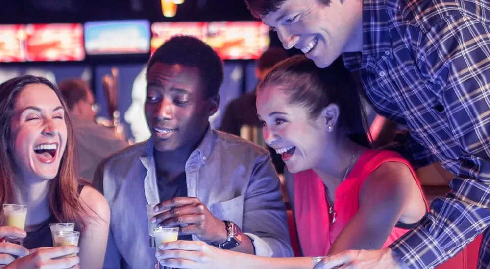 Four friends laughing and drinking shots together in a bar.