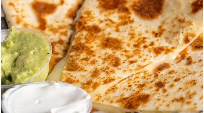 Toasted quesadilla triangles with visible melted cheese, guacamole, and sour cream.