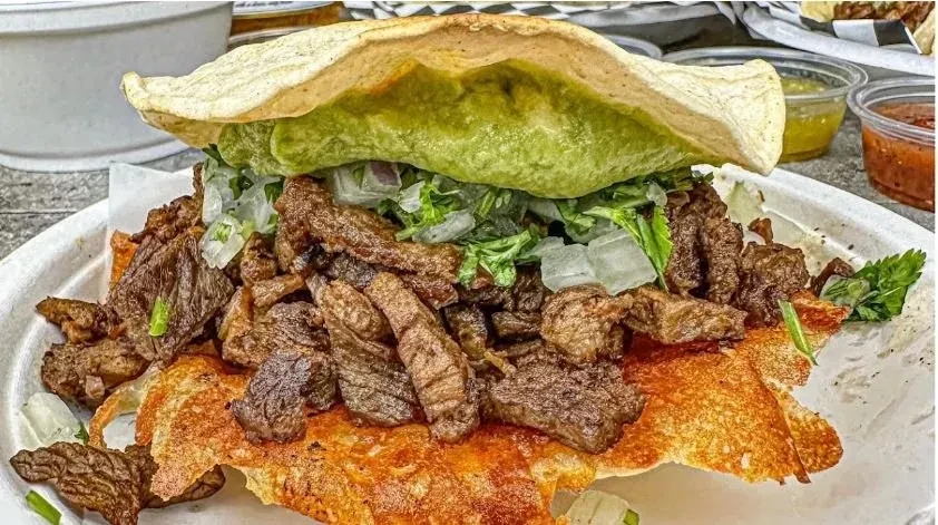 Large open-faced taco with grilled meat, onions, lettuce, and guacamole.