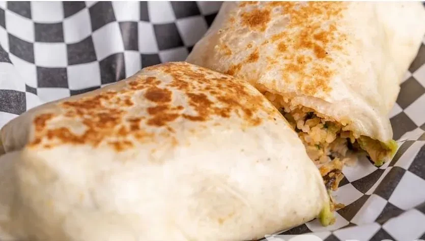 Two toasted burritos with rice filling on checkered paper.
