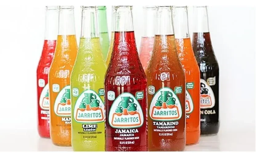 A row of eight colorful Jarritos soda bottles on white.