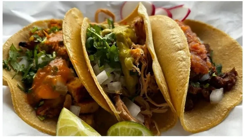 Three meat tacos on corn tortillas with salsa, guacamole, and lime.