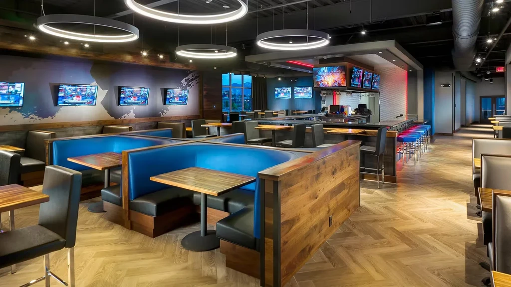 Modern, empty sports bar with blue booths, bar, herringbone floor, multiple TVs.