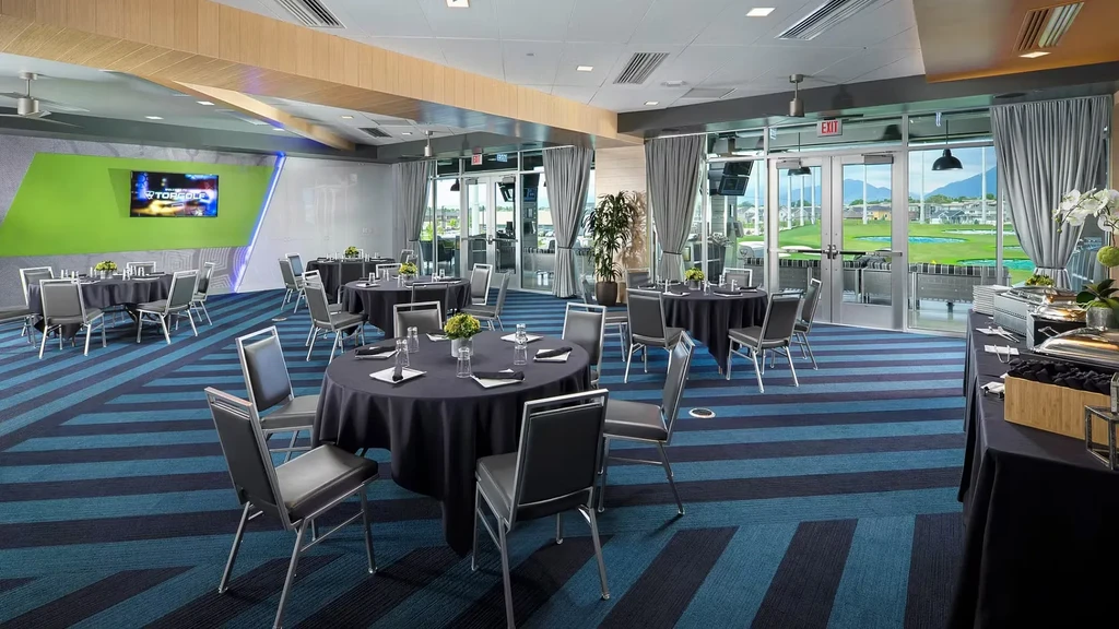 Modern TOPGOLF event room with tables, buffet, and golf range view.