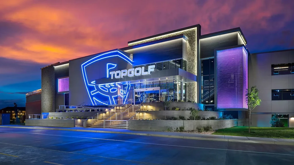 Modern Topgolf building exterior illuminated in blue and purple at dusk.