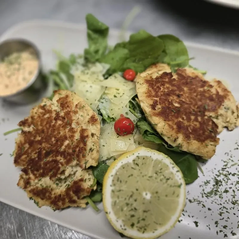 Two golden-brown patties on greens with cheese, sauce, and lemon.