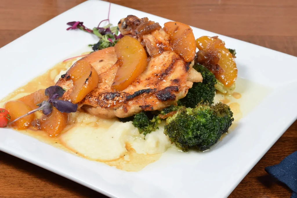 Grilled chicken breast with glazed fruit, mashed potatoes, and broccoli.