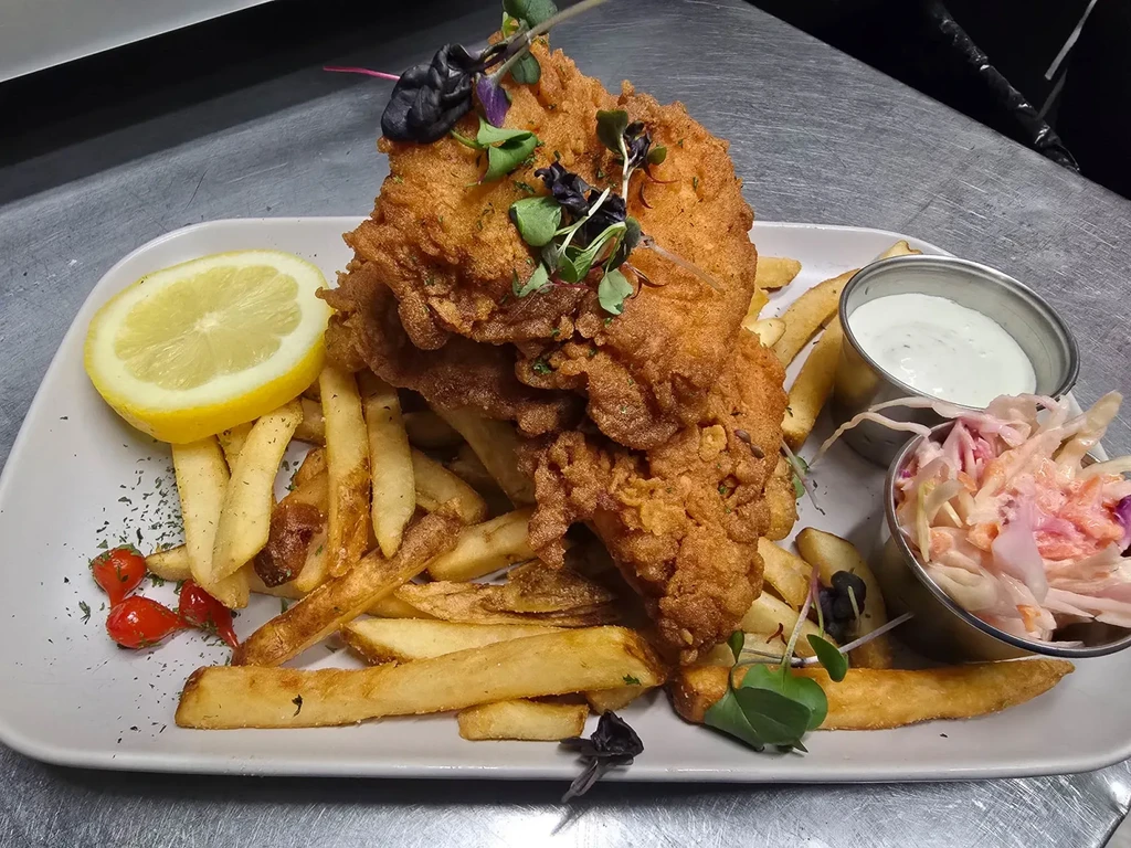 Crispy fried chicken/fish, french fries, coleslaw, sauce, and lemon on plate.