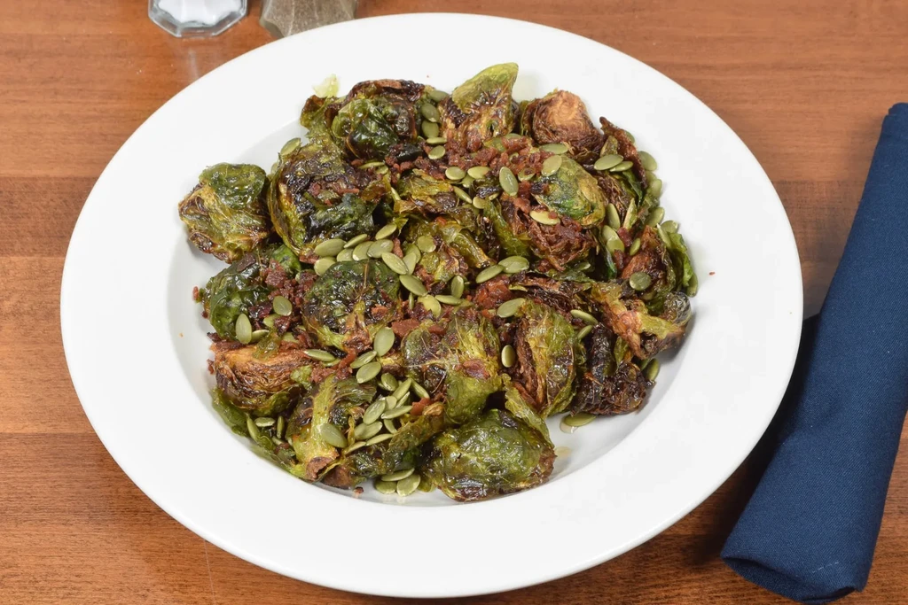 Charred Brussels sprouts with pepitas and dark seasoning in a white bowl.