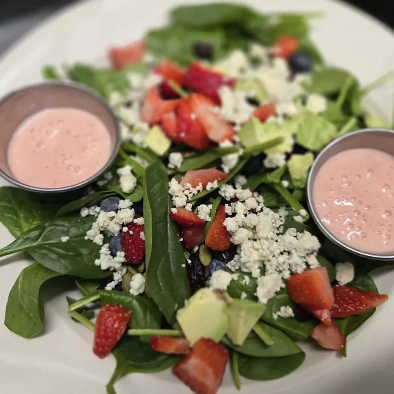 Salad with spinach, strawberries, blueberries, avocado, feta, and pink dressing.