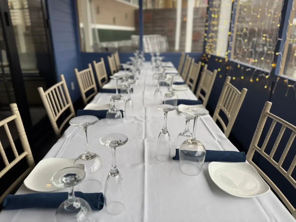 Outdoor restaurant table set with white plates, blue napkins, warm string lights.
