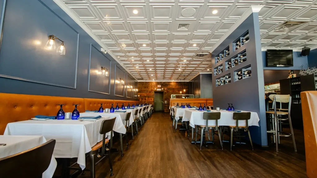 Modern restaurant interior featuring long dining area, banquette, and patterned tin ceiling.