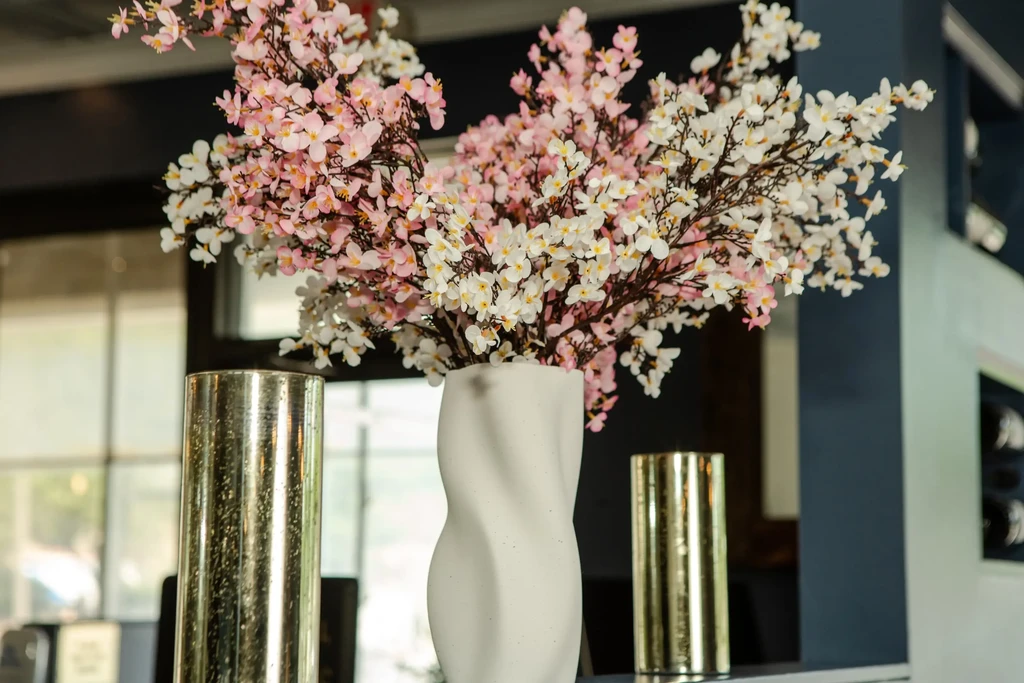 Artificial cherry blossoms in a twisted vase, flanked by golden cylinders.