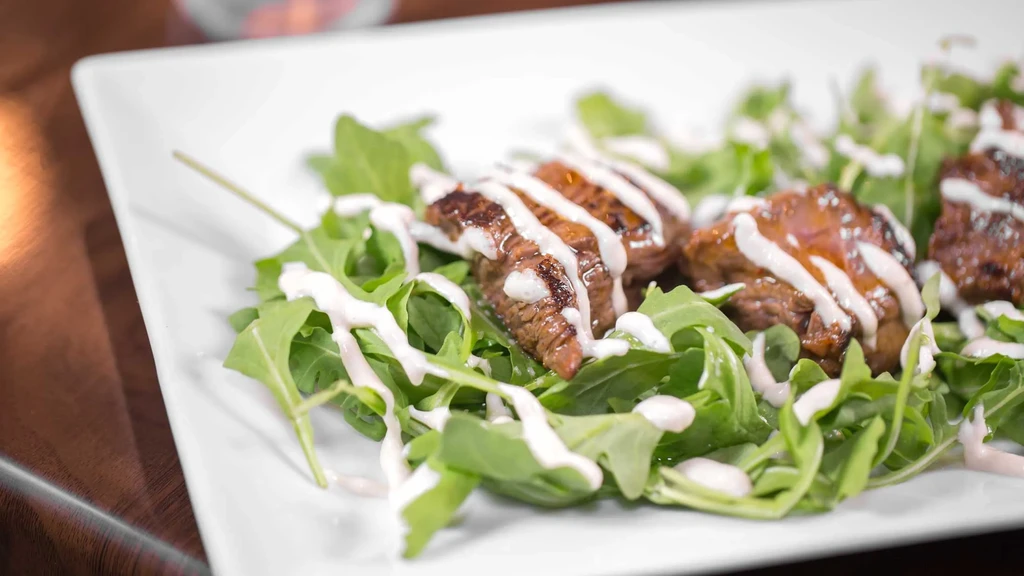 Professionally plated grilled meat, arugula, and creamy sauce.