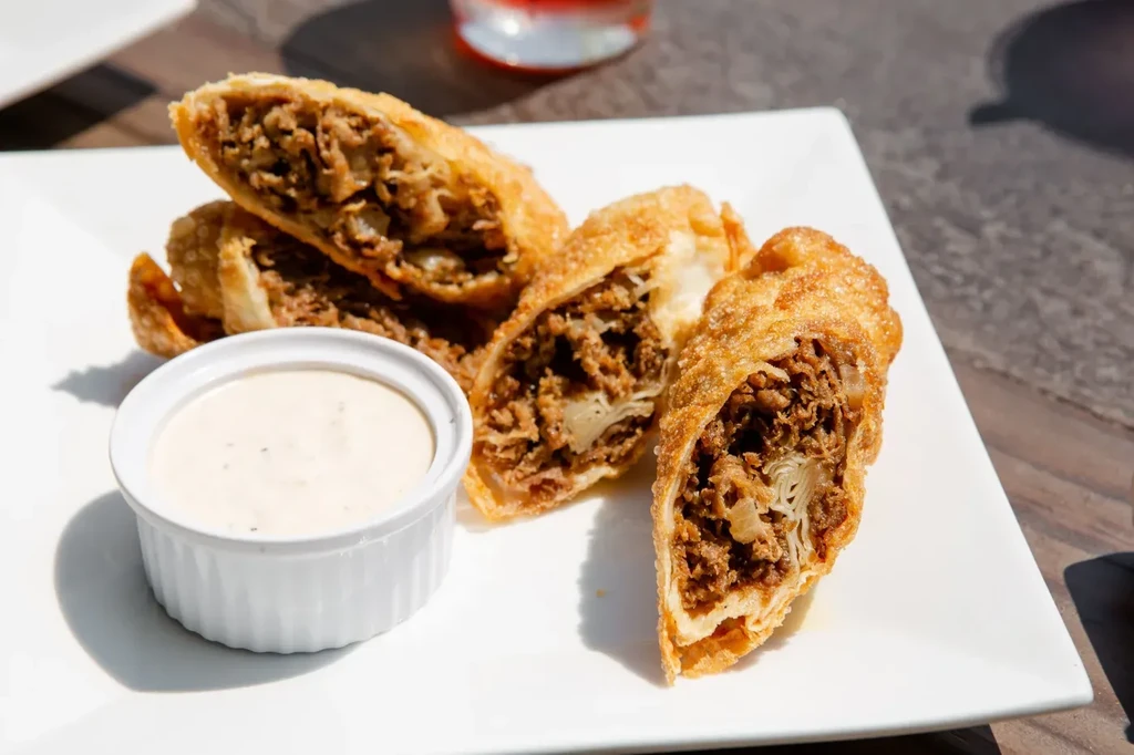 Cut deep-fried rolls show savory meat filling and dipping sauce.