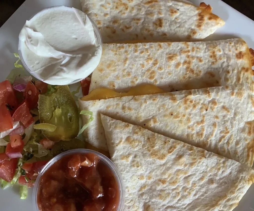 Close-up: cheese quesadillas with sour cream, salsa, and fresh vegetables.