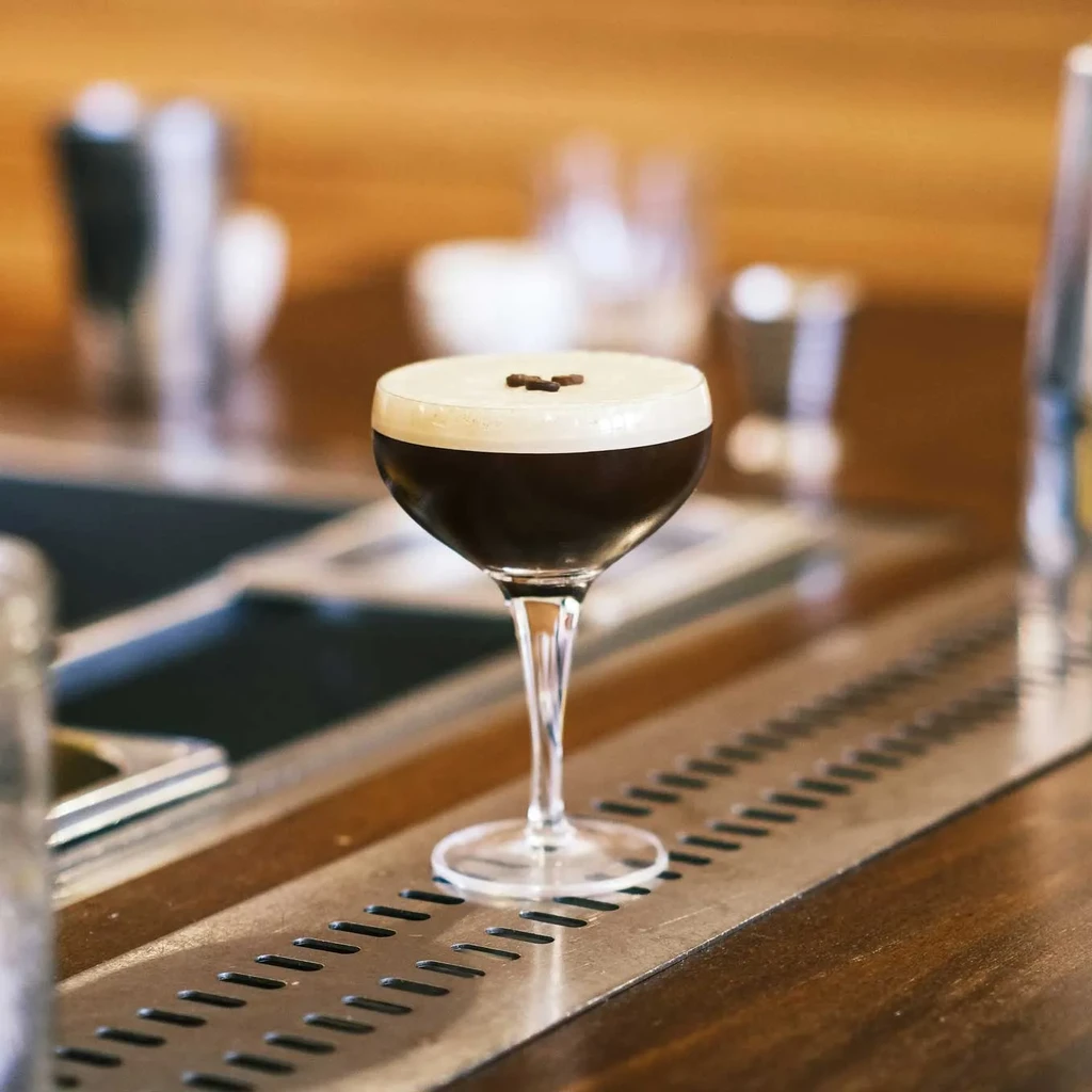 Espresso Martini in a coupe glass with coffee beans on a wooden bar.
