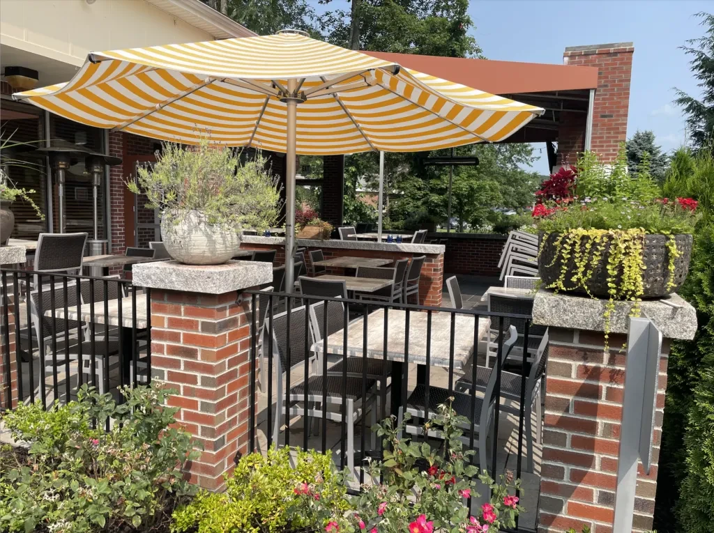 Sunny restaurant patio with yellow striped umbrella, tables, and plants.