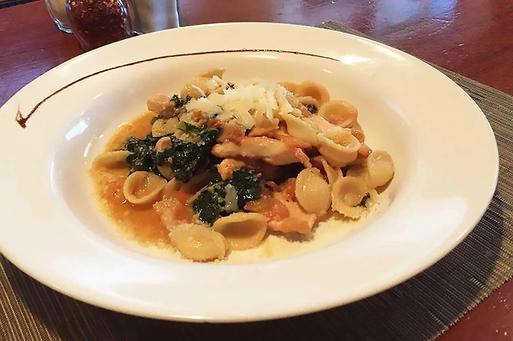 Orecchiette pasta with chicken, greens, red sauce, and cheese.