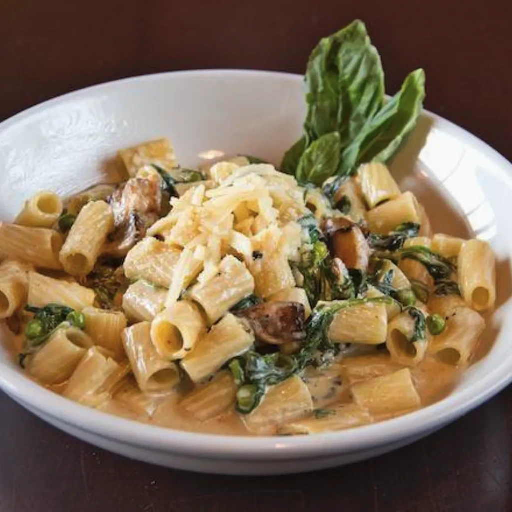 Creamy rigatoni pasta with mushrooms, spinach, peas, Parmesan, and fresh basil.