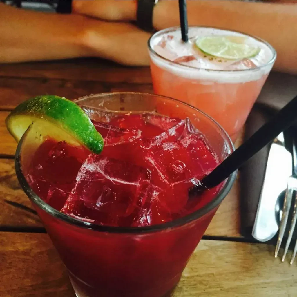 Dark red and pink cocktails with lime and straws on a wooden table.