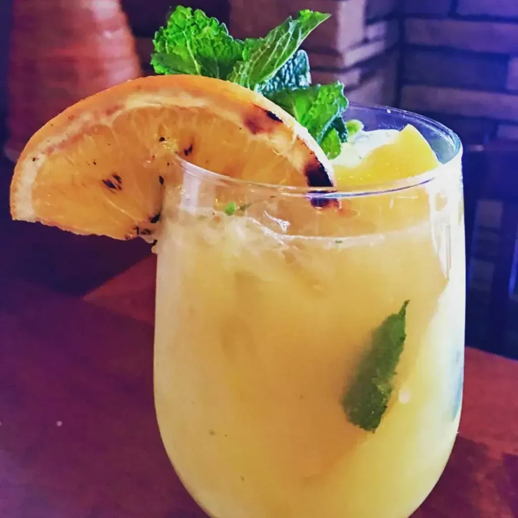 Yellow-orange drink with grilled orange slice and fresh mint.