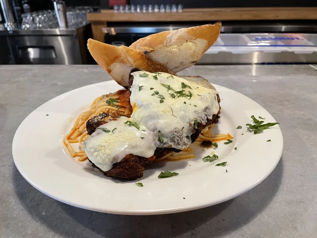 Plated chicken parmesan with spaghetti, melted cheese, herbs, and bread.