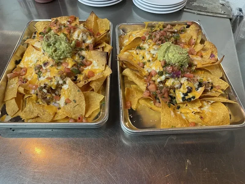 Two trays of nachos with melted cheese, guacamole, salsa, meat, and beans.