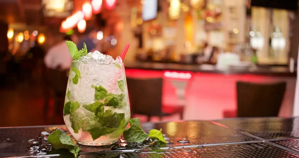 Mint cocktail with ice and red straw on a bar.