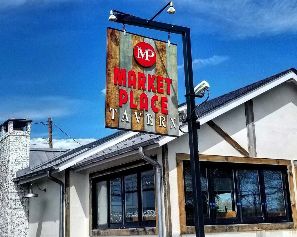 Rustic "MARKET PLACE TAVERN" sign and building under a blue sky.