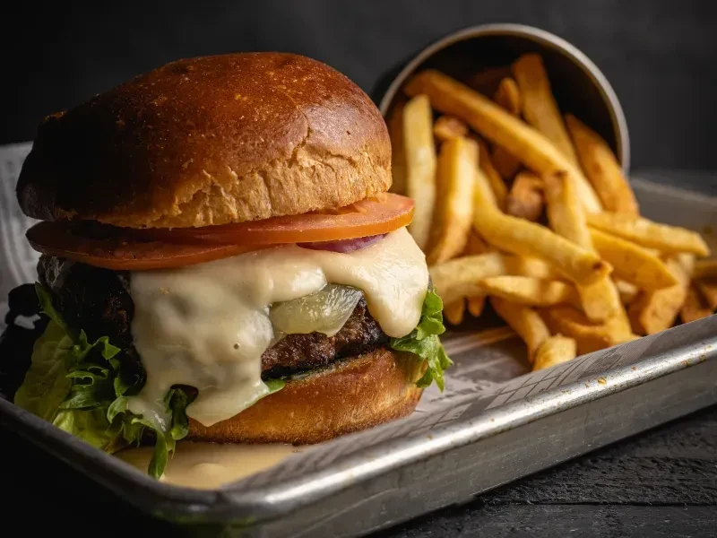 Hamburger with cheese, lettuce, tomato, and golden french fries on a tray.