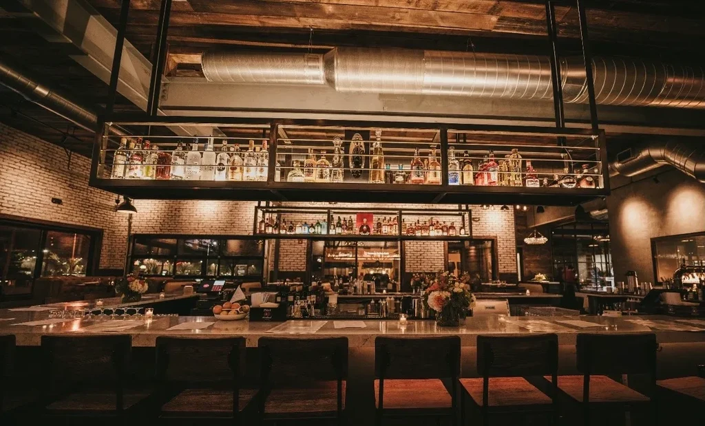 Upscale industrial-chic bar with well-stocked counter and glowing liquor bottles.