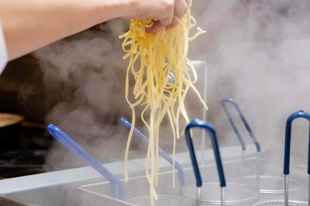 Hand holding steaming yellow pasta over a kitchen steaming station.