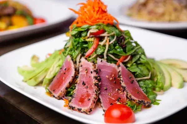 Close-up of seared sesame tuna salad with greens, avocado, and vegetables.