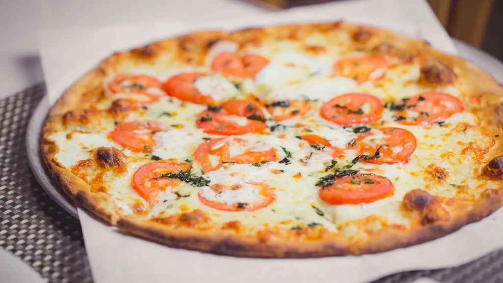 Freshly baked Margherita pizza with mozzarella, tomato, and basil on a tray.