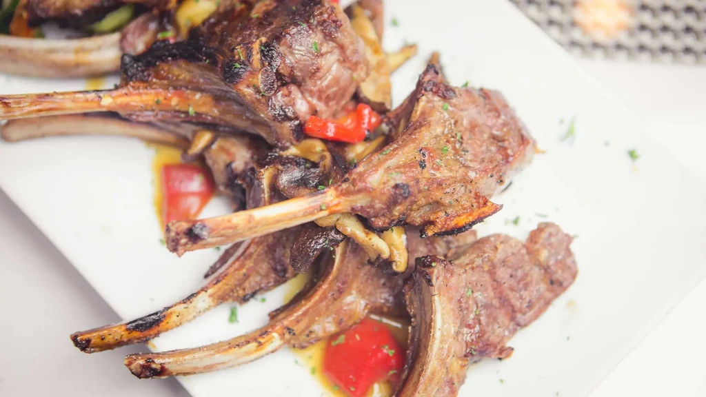 Grilled lamb chops, bell peppers, mushrooms, and savory sauce on a plate.