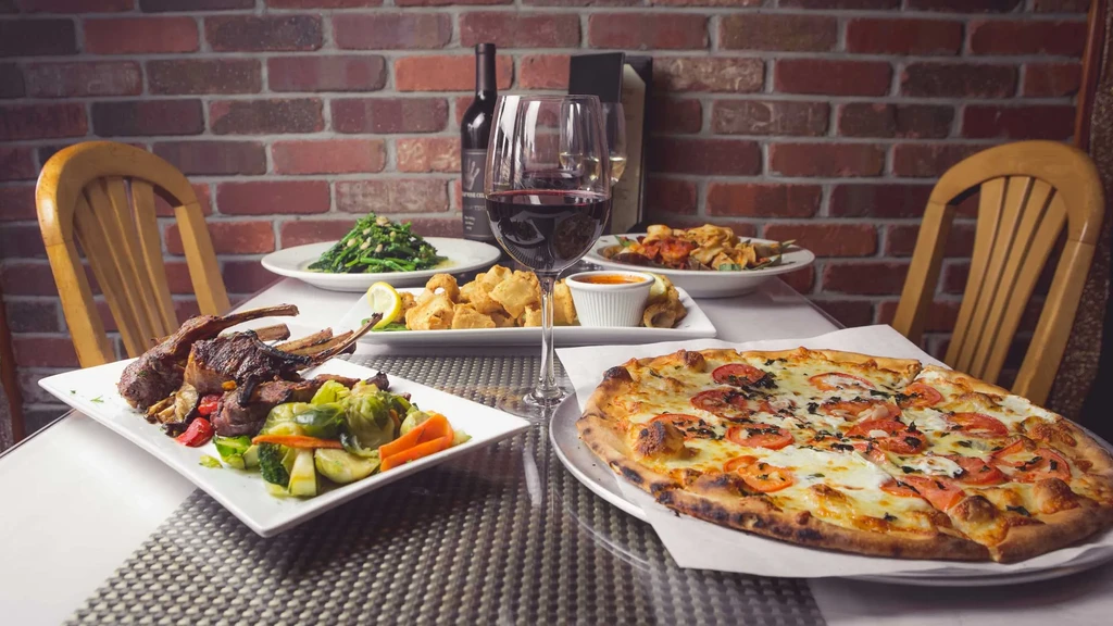 Restaurant table with pizza, lamb chops, fried seafood, and red wine.