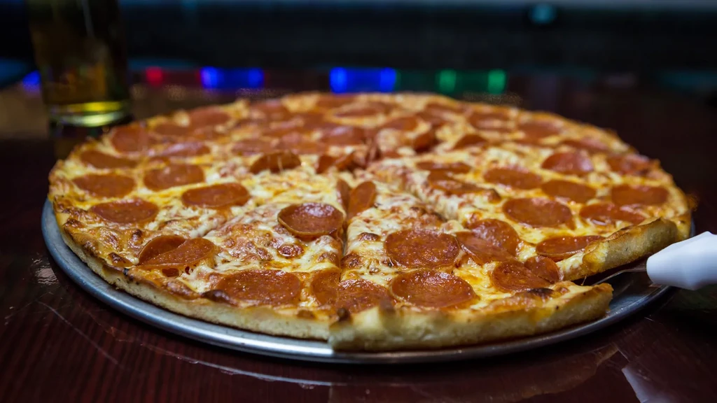 A large pepperoni pizza on a metal pan with a slice being removed.