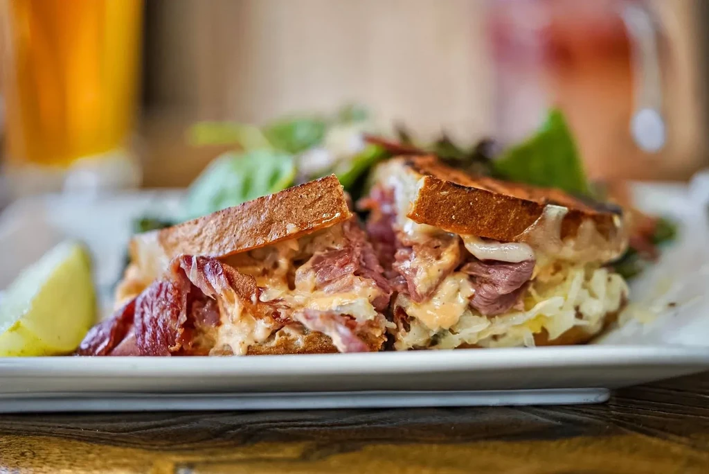 A cut Reuben sandwich with sauerkraut and melted cheese on a white plate.