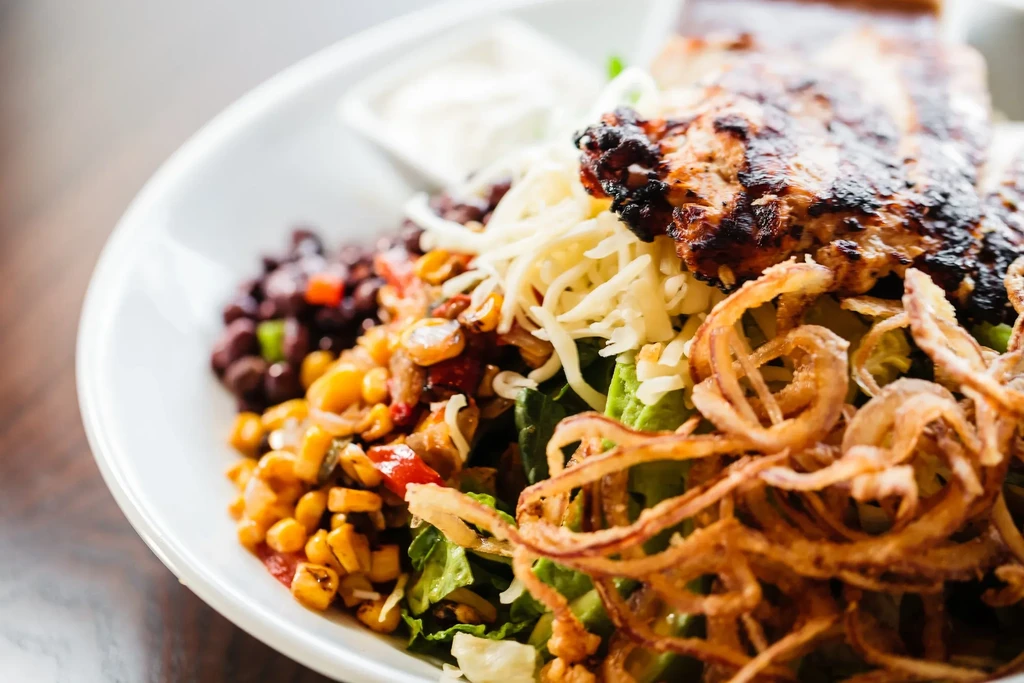 A close-up of a salad with grilled chicken, corn, black beans, and crispy onions.