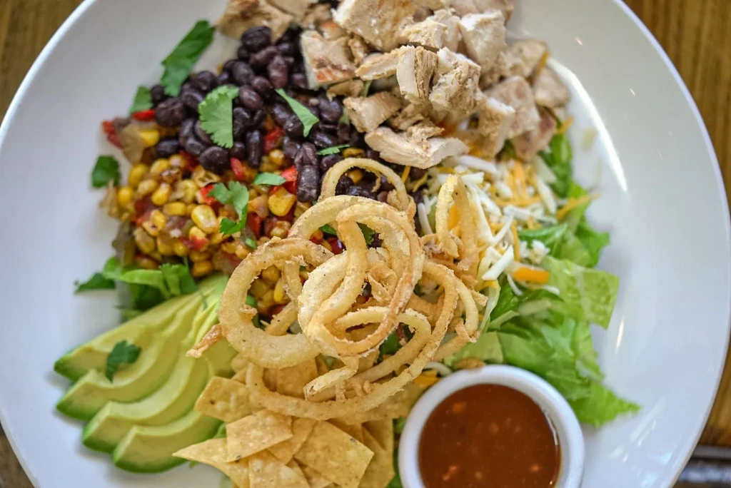 Chicken salad with black beans, corn, avocado, onion rings, and salsa.