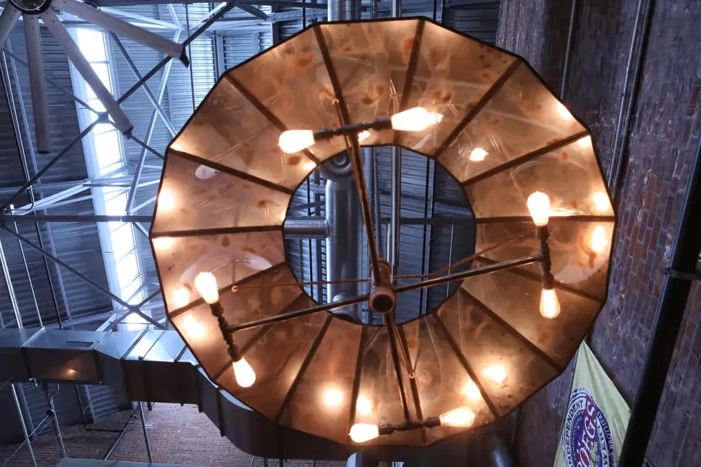 A circular chandelier hangs from an industrial ceiling with exposed beams and ductwork.