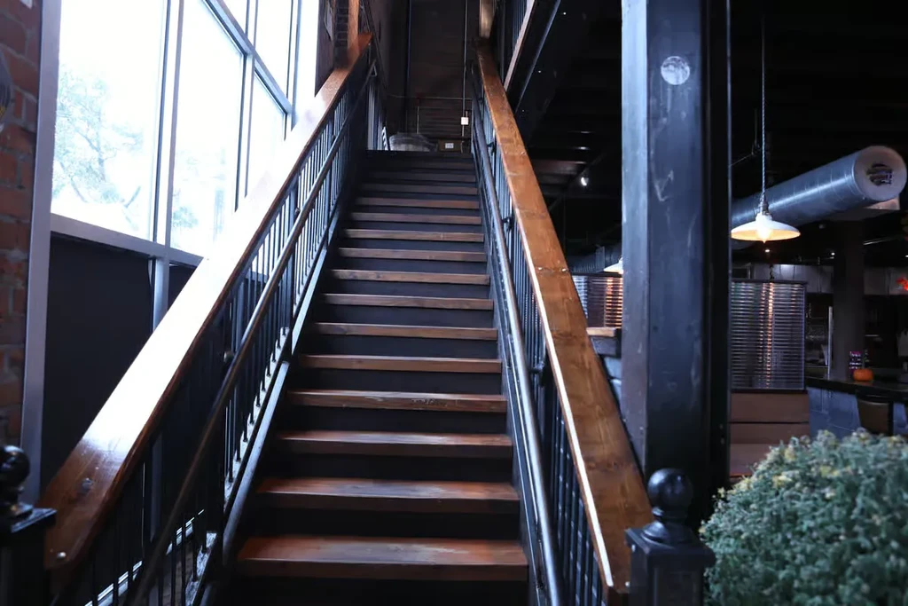 A long wooden staircase with black risers, a large window on the left.