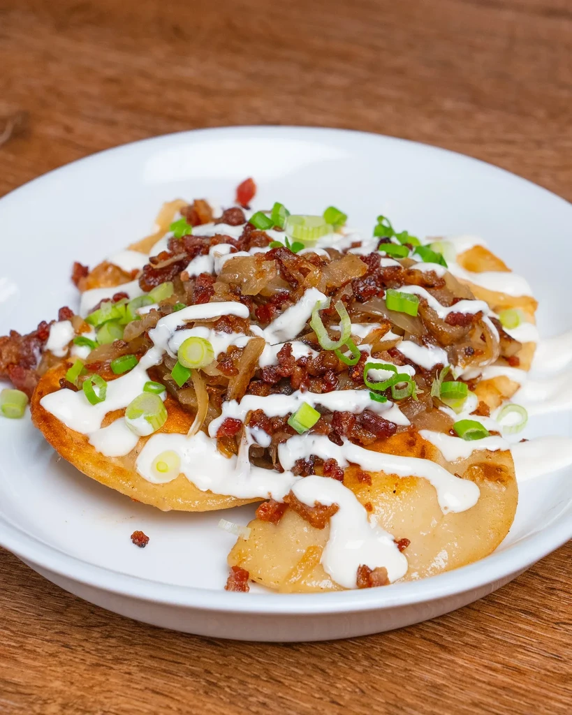 Pierogi with fried onions, bacon bits, and sour cream on a white plate.