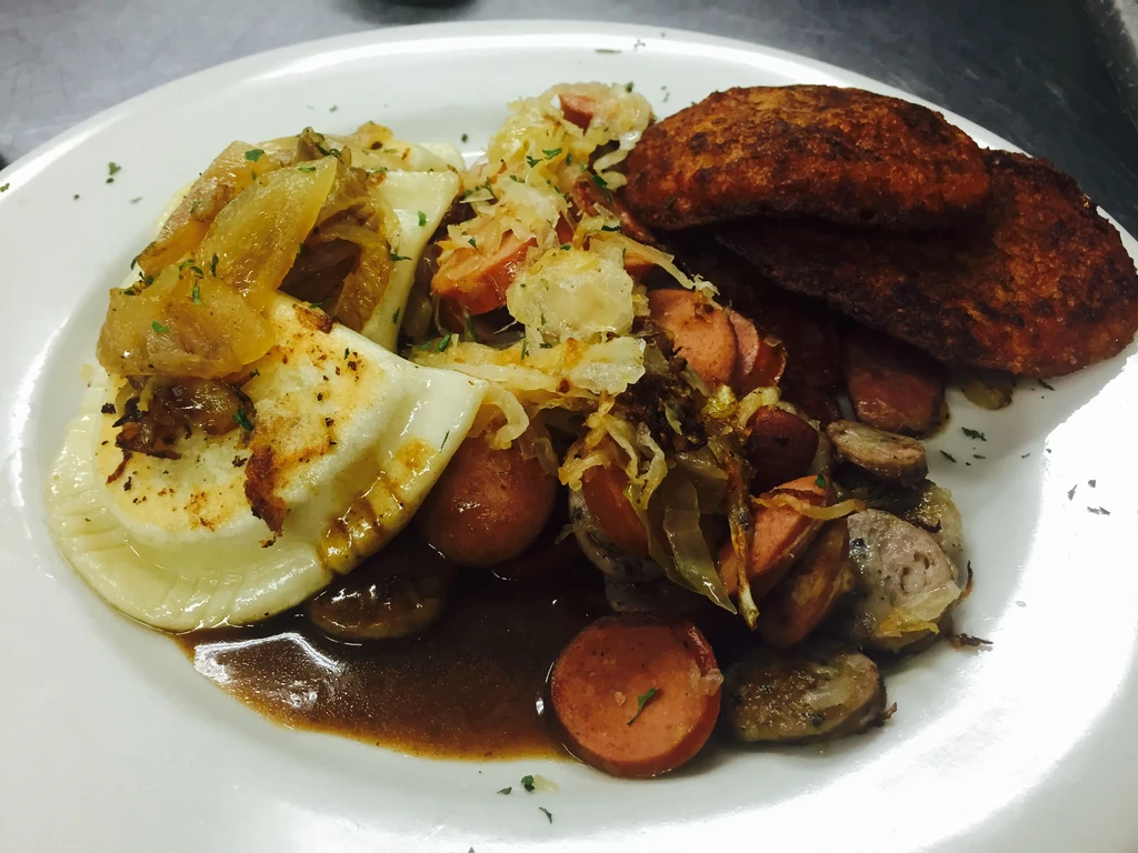 A plate of pierogi, sausages, fried onions, sauerkraut, and potato pancakes.