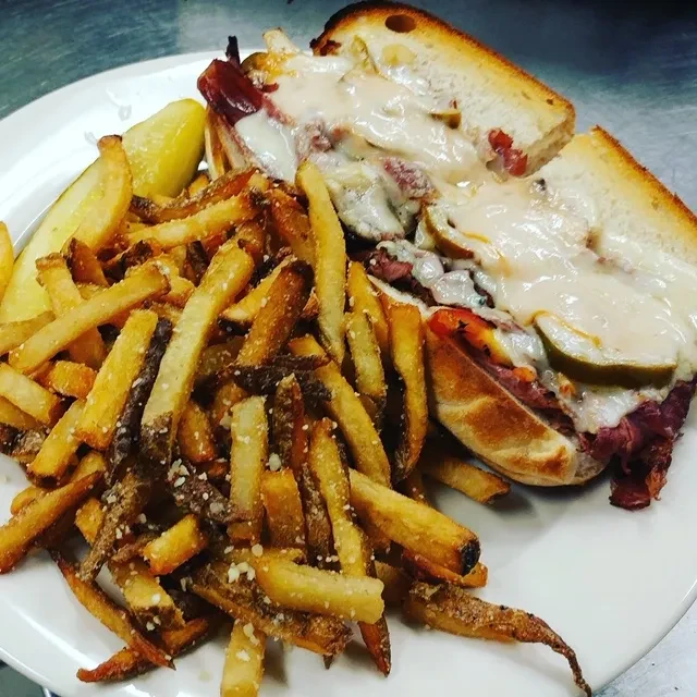 A large portion of golden french fries and a pastrami sandwich.